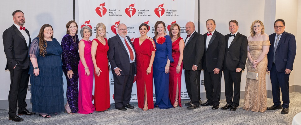 Large group of people in formal dress in front of American Heart Association step and repeat banner.